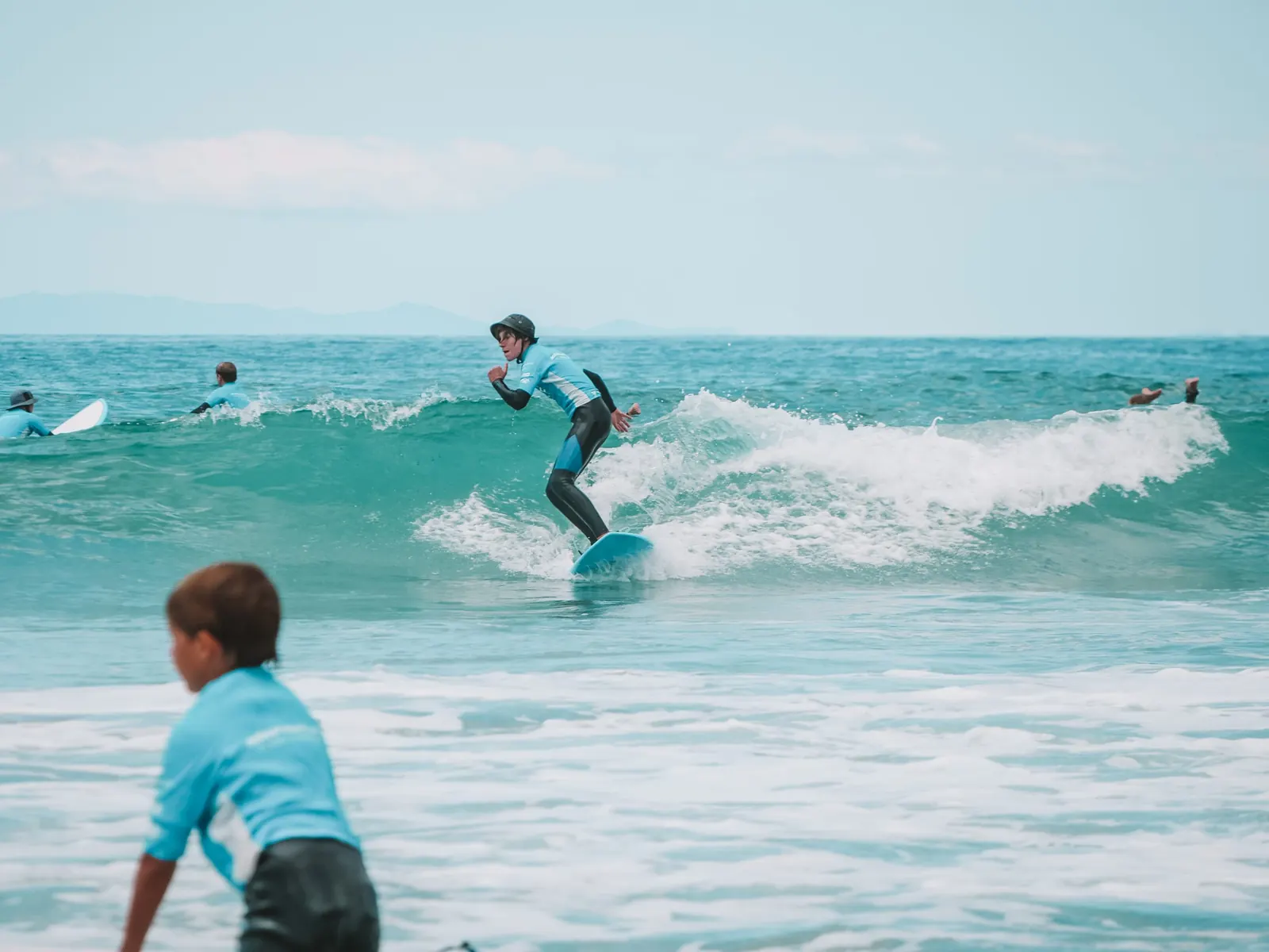 A student trims along a small wave at Orewa Beach