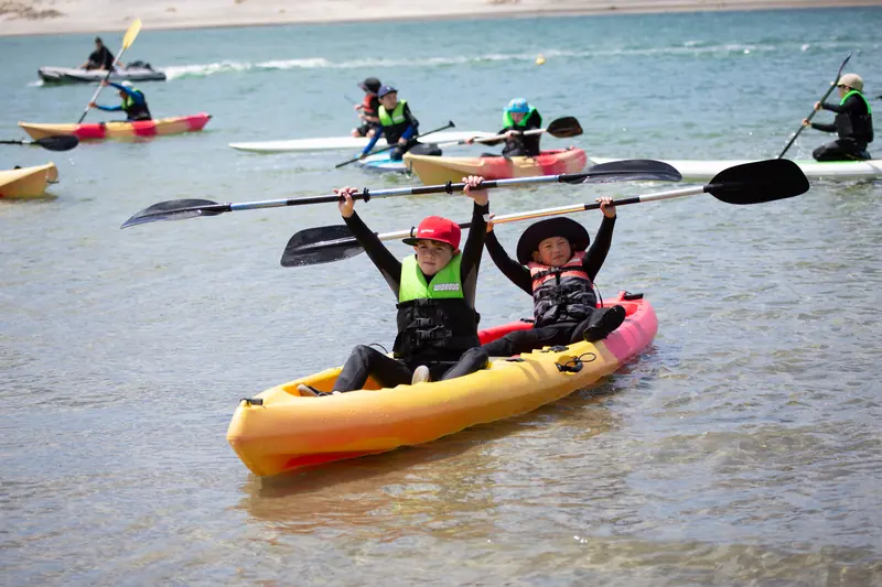 Students raise their paddles from kayaks on the sheltered estuary