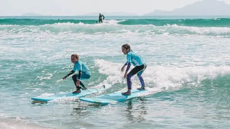 Two students ride side-by-side waves in matching blue rash shirts