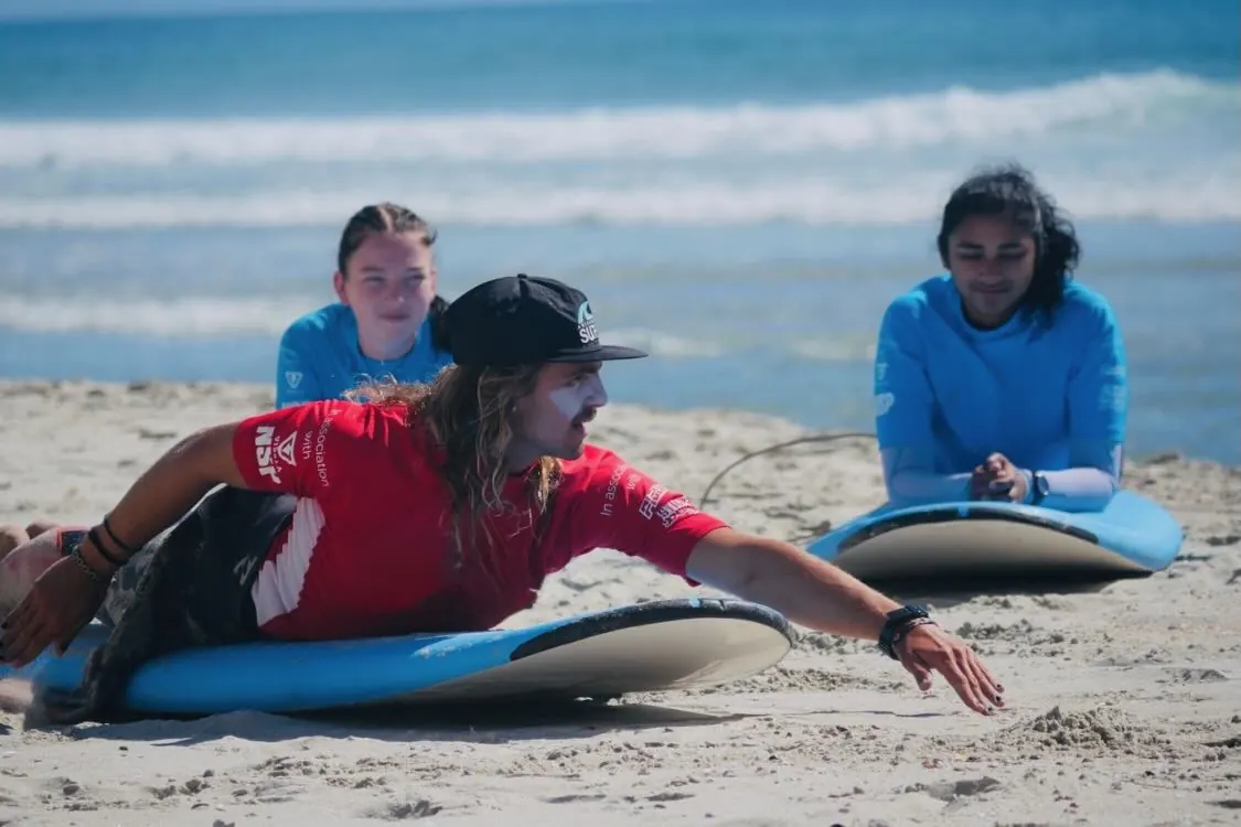 A group surf lesson warming up on the sand with instructors at Orewa Beach