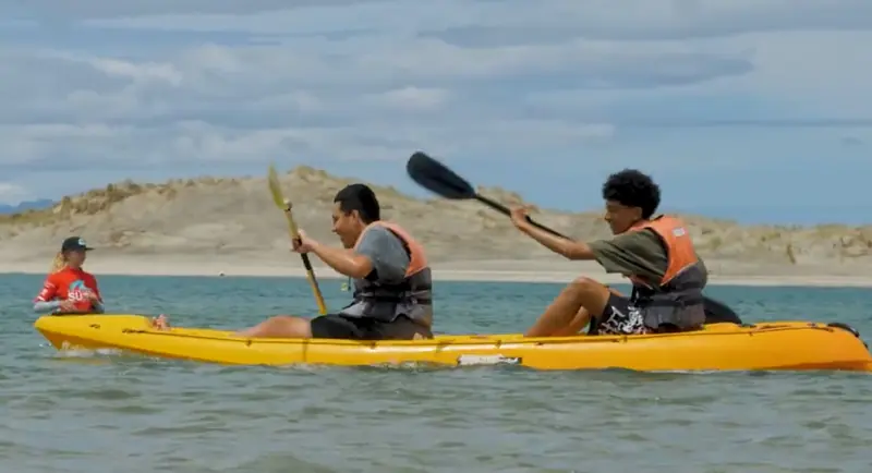 Two campers paddle a tandem kayak across the Mangawhai estuary