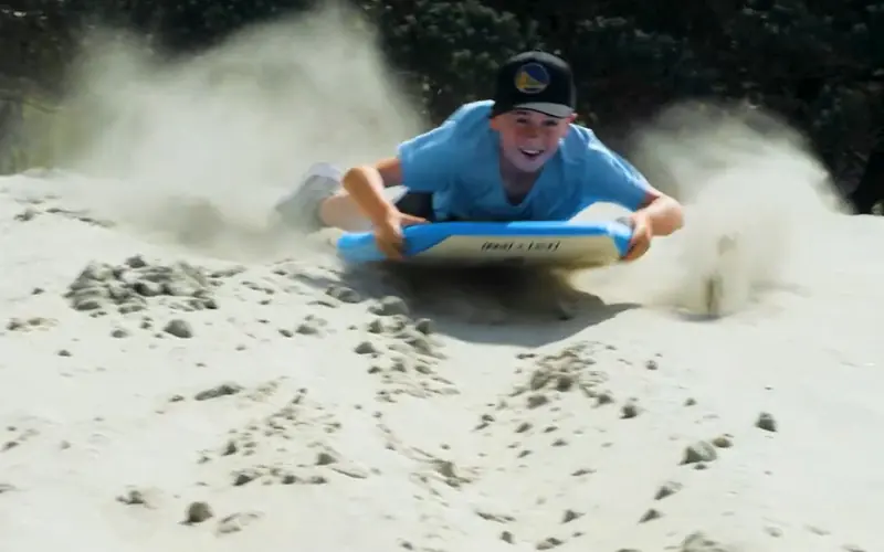 A camper flies down the dunes face-first on a sandboard