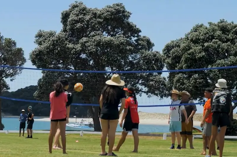 Campers play volleyball on the grass beside the estuary