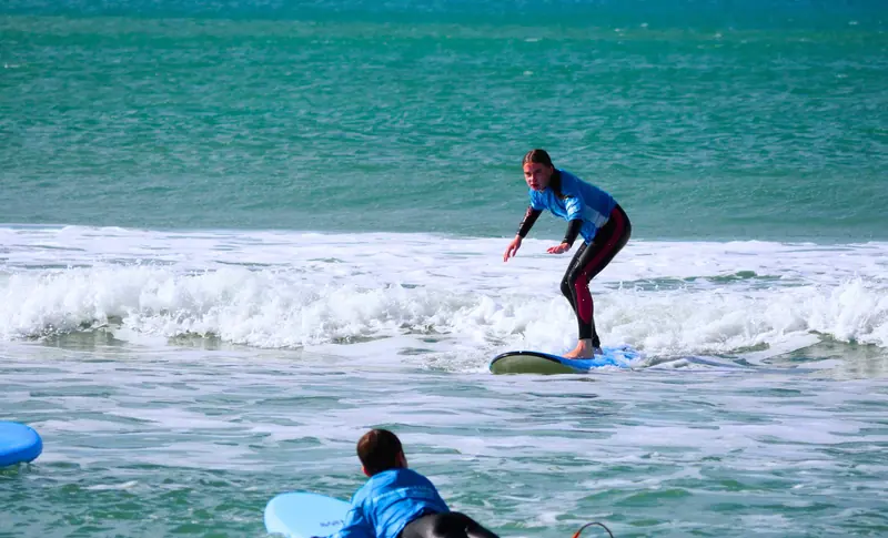 A student rides a green wave at Orewa while classmates paddle out