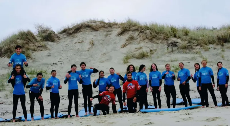 A full secondary group in blue rash shirts lines up on the sand at Te Arai