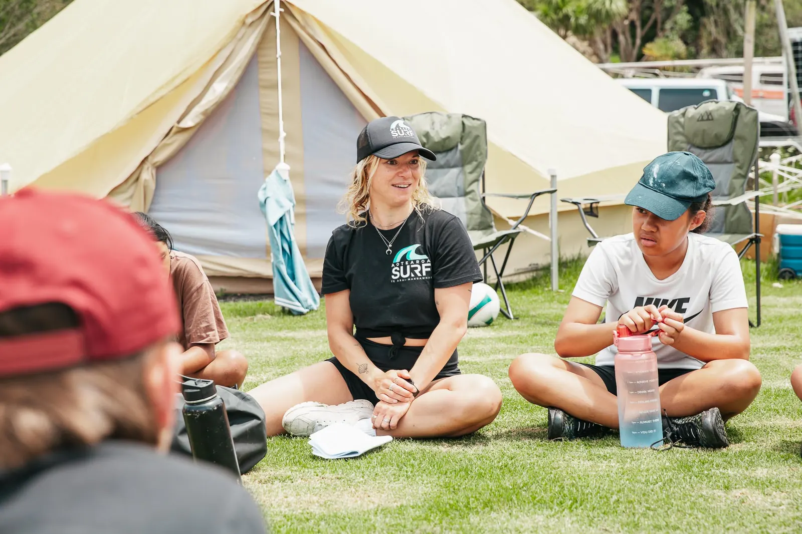 Group leaders relax on the grass in front of the glamping teepees