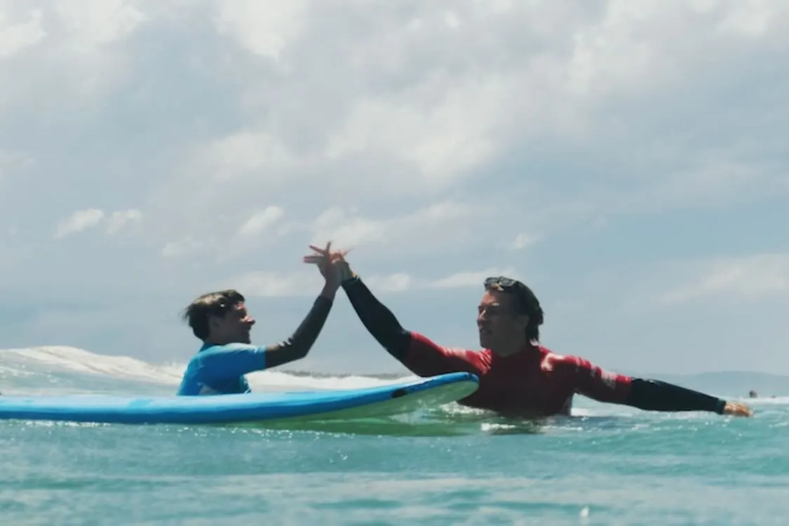 An instructor and student high-five between waves